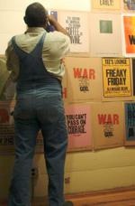 Amos Kennedy stands in front of a wall of prints with his back to the camera