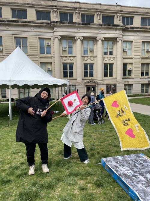 Two Japanese papermakers stand on the UI Pentacrest with Earth Day flags