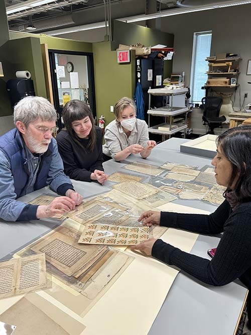 A group of people stand around a table looking at Islamic manuscripts