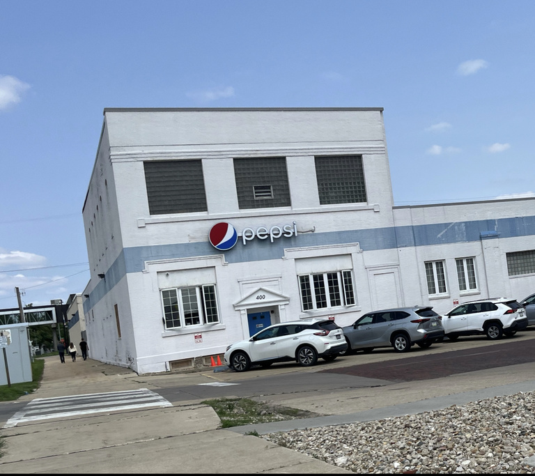 a white building with a pepsi sign with cars in front of it