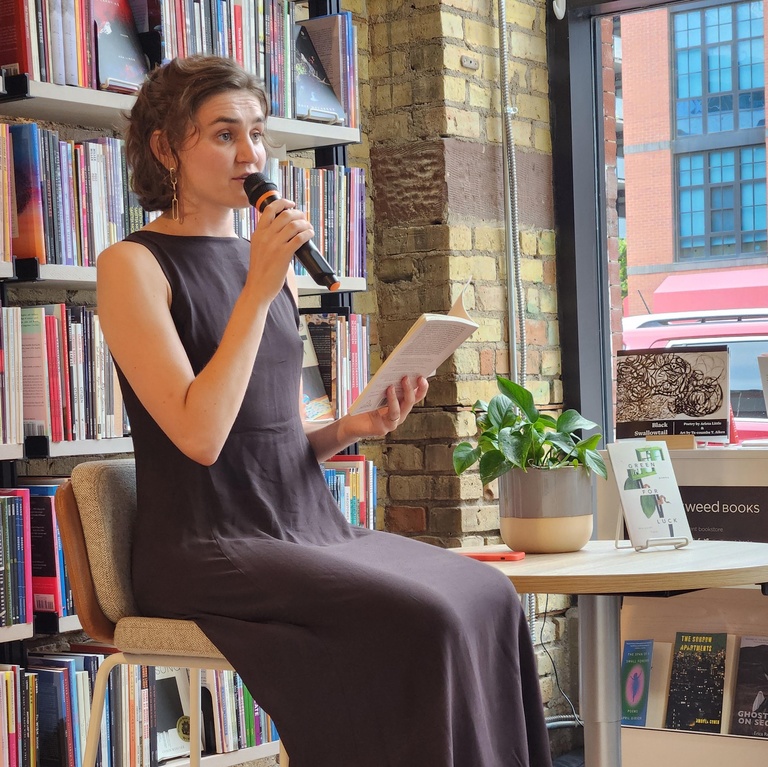 Woman dressed in black holding a microphone and reading from a book