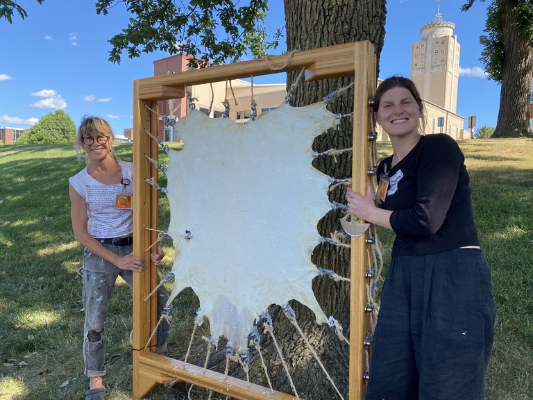 two women standing by a scraped and stretched goat skin