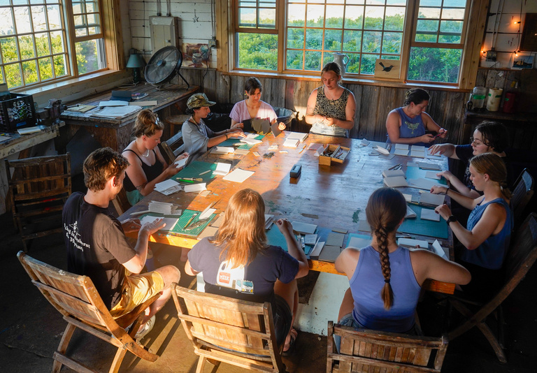 Oliver teaching a book binding workshop, surrounded by students.