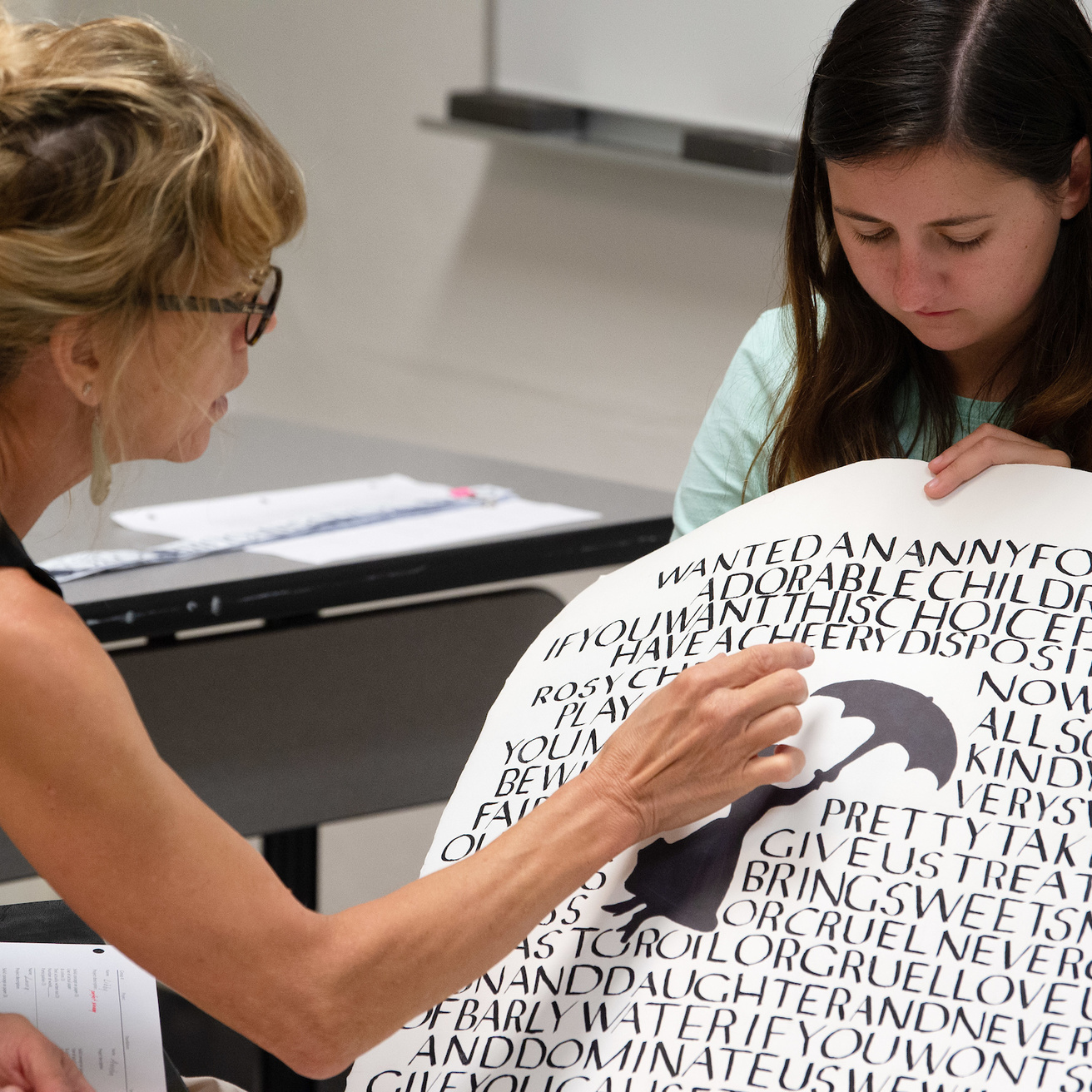 A woman holds up a poster with calligraphy on it and another woman examines it