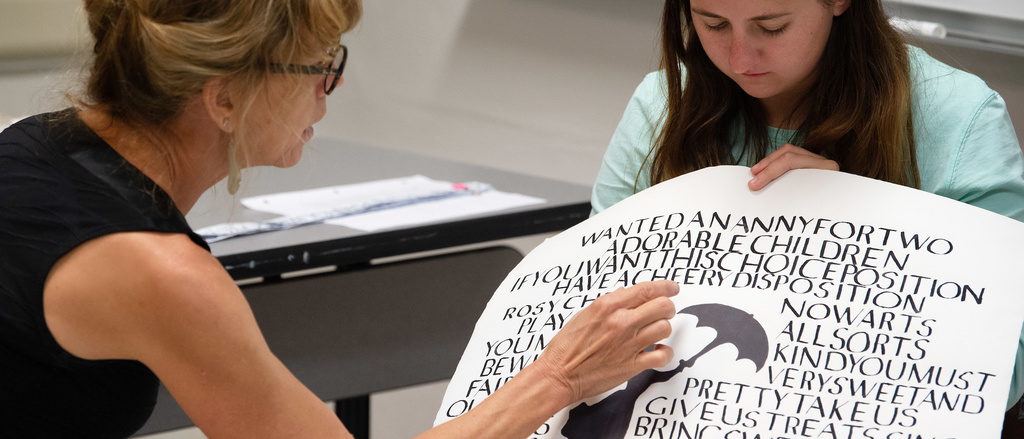 A woman holds up a poster with calligraphy on it and another woman examines it
