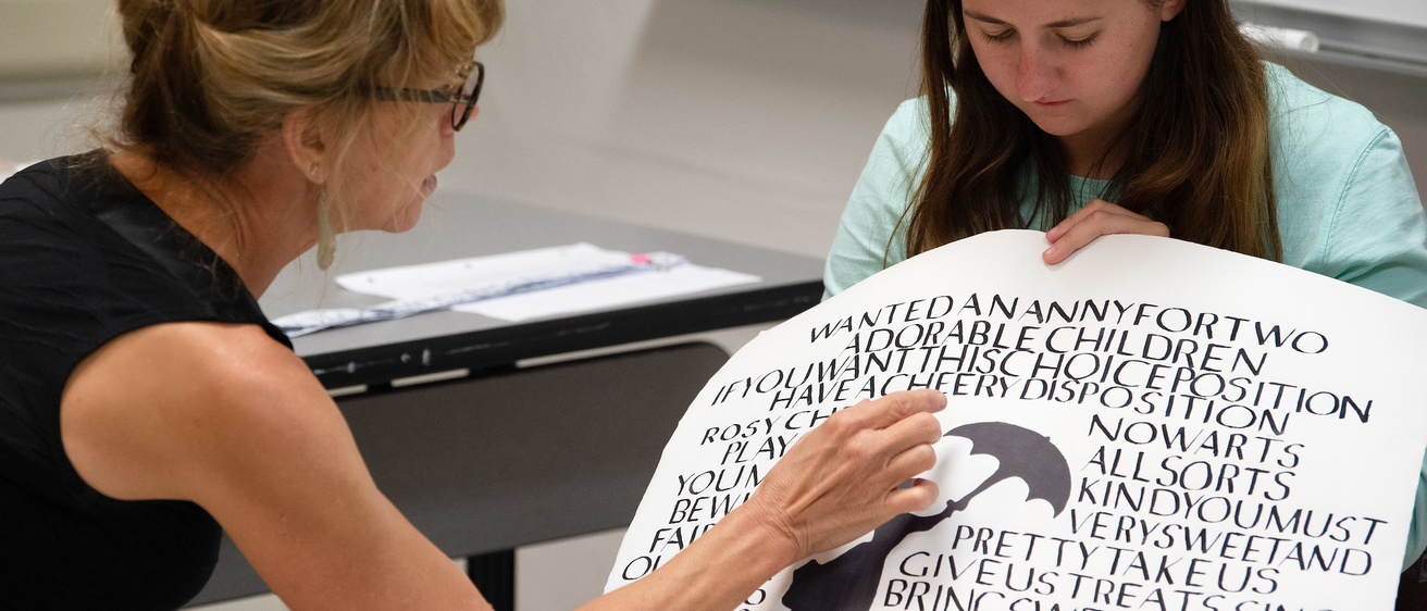 A woman holds up a poster with calligraphy on it and another woman examines it